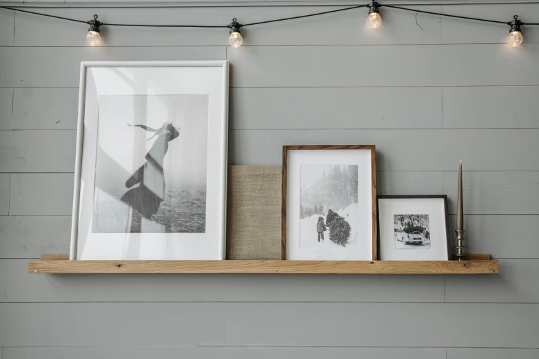 a couple of pictures sitting on top of a wooden shelf, a black and white photo, inspired by Andrew Wyeth, featured on unsplash, visual art, light grey backdrop, hessian cloth, multiple lights, simple wood shelves