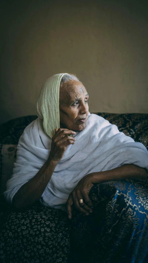 a woman sitting on top of a couch covered in a blanket, a portrait, inspired by Gordon Parks, unsplash contest winner, hurufiyya, ethiopian, nursing home, 15081959 21121991 01012000 4k, calmly conversing 8k