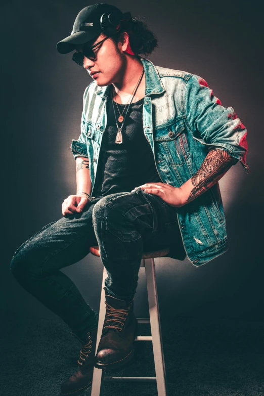 a man sitting on top of a wooden stool, an album cover, inspired by Randy Vargas, trending on pexels, wearing a jeans jackets, inked, androgynous male, profile image