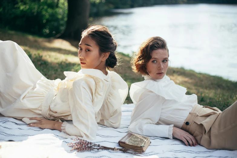 a couple of women laying on top of a blanket, an album cover, inspired by Konstantin Somov, trending on pexels, baroque, wearing lab coat and a blouse, sydney park, maggie cheung, at the waterside