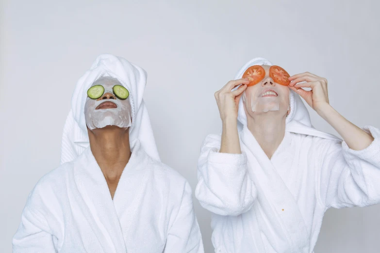 two women with facial masks and cucumbers on their faces, trending on pexels, white robe, fun pose, background image, ivy's