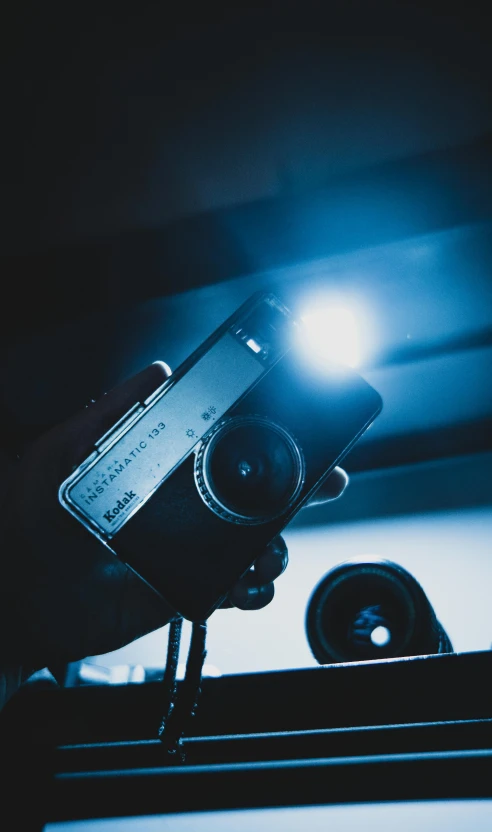 a close up of a person holding a camera, inspired by Elsa Bleda, blue lighting, flashlight on, film quality, cinematic. by leng jun