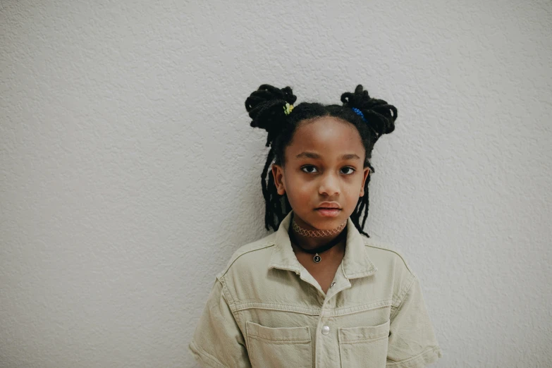 a little girl standing in front of a white wall, pexels contest winner, afrofuturism, with dark hair tied up in a bun, androgynous person, 15081959 21121991 01012000 4k, dreadlock black hair