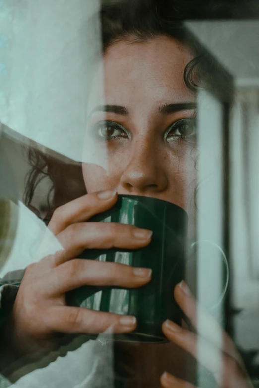 a close up of a person holding a cup, by Adam Marczyński, pexels contest winner, pouty face, green light coming from window, faces of too much caffeine, young woman's face