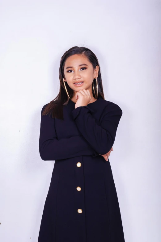 a woman standing in front of a white wall, an album cover, isabela moner, wearing black coat, ariana grande photography, solid background