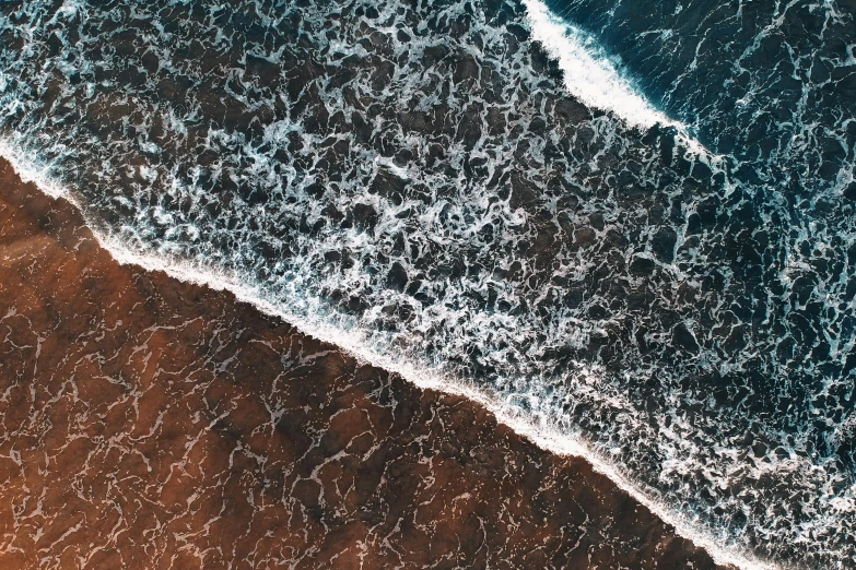 a person riding a surfboard on top of a sandy beach, a microscopic photo, by Daniel Lieske, unsplash contest winner, analytical art, aerial shot from the drone, both bright and earth colors, ocean spray, view of sea