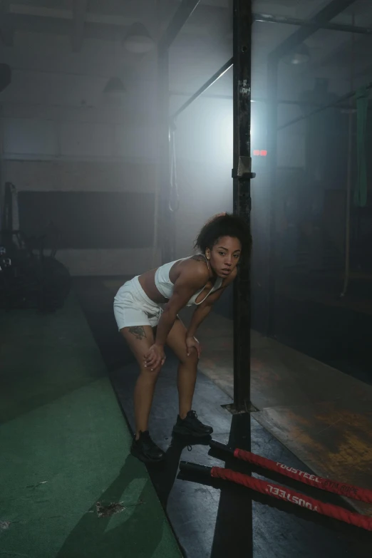 a woman leaning against a pole in a dark room, in a gym, ashteroth, bra and shorts streetwear, concerned expression