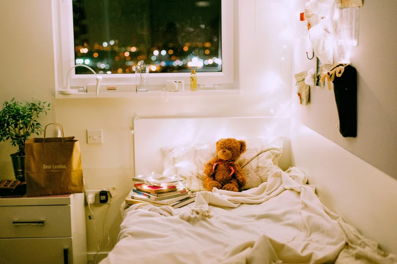 a teddy bear sitting on top of a bed next to a window, a cartoon, inspired by Elsa Bleda, pexels contest winner, fairy lights, small and cosy student bedroom, someone in home sits in bed, white bed