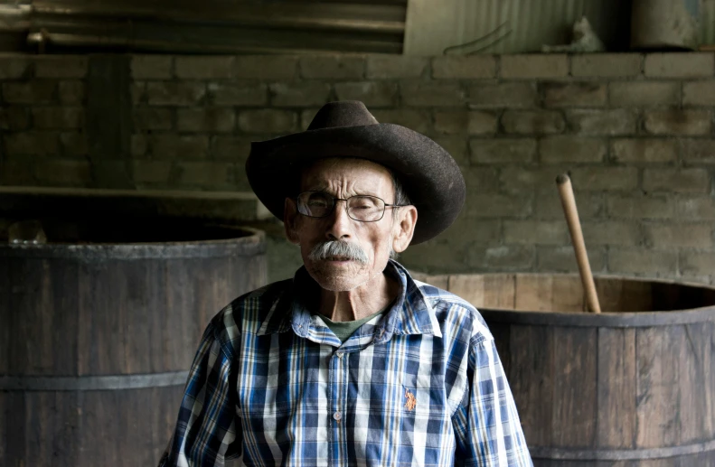 a man in a cowboy hat standing in front of barrels, a portrait, pexels contest winner, oldman with mustach, ute osterwalder, sydney hanson, taken in the late 2010s