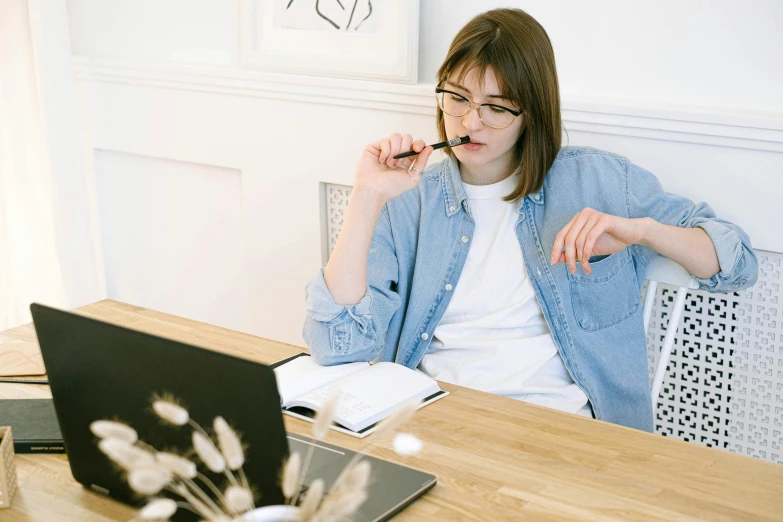 a woman sitting at a table in front of a laptop, by Nicolette Macnamara, trending on pexels, holding pencil, with square glasses, casey cooke, smoking a joint