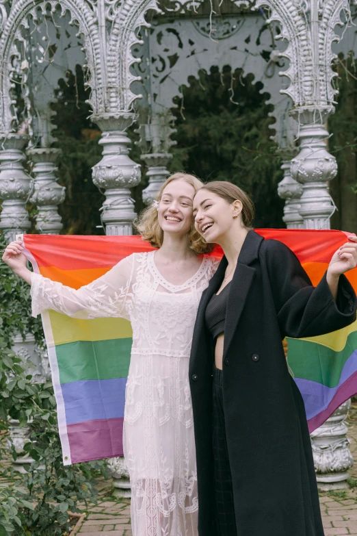 a couple of women standing next to each other holding a rainbow flag, by Julia Pishtar, low quality photo, irina french, pale - skinned, ad image