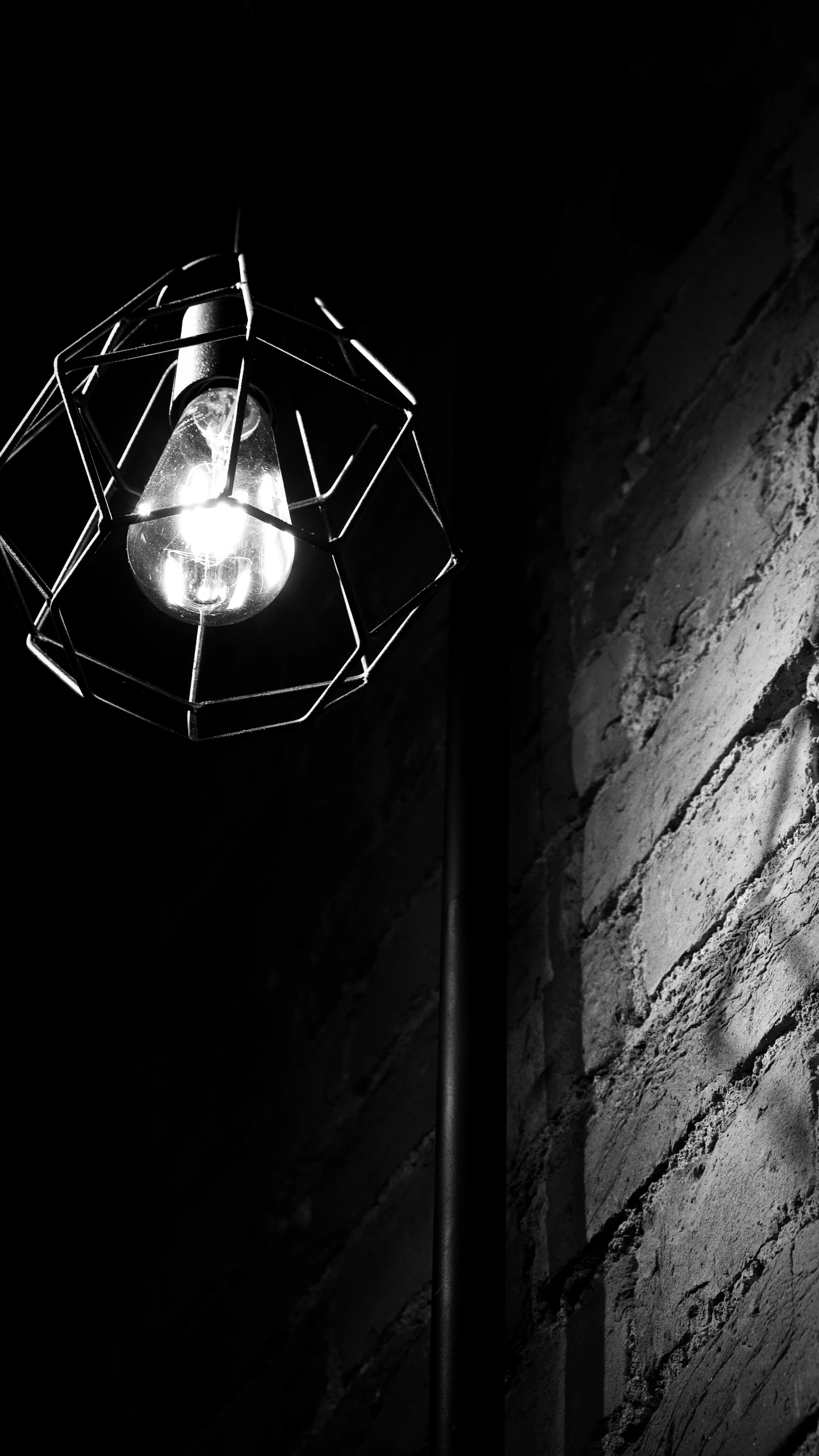 a black and white photo of a light on a brick wall, inspired by Brassaï, pexels, light and space, attached to wires. dark, lightbulb, high details photo