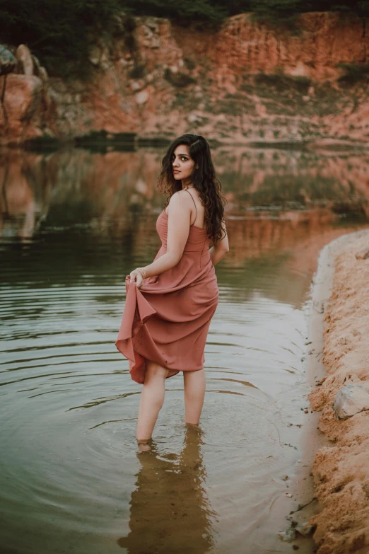 a woman standing in a body of water, in a dusty red desert, wearing a dress, promo image, near pond