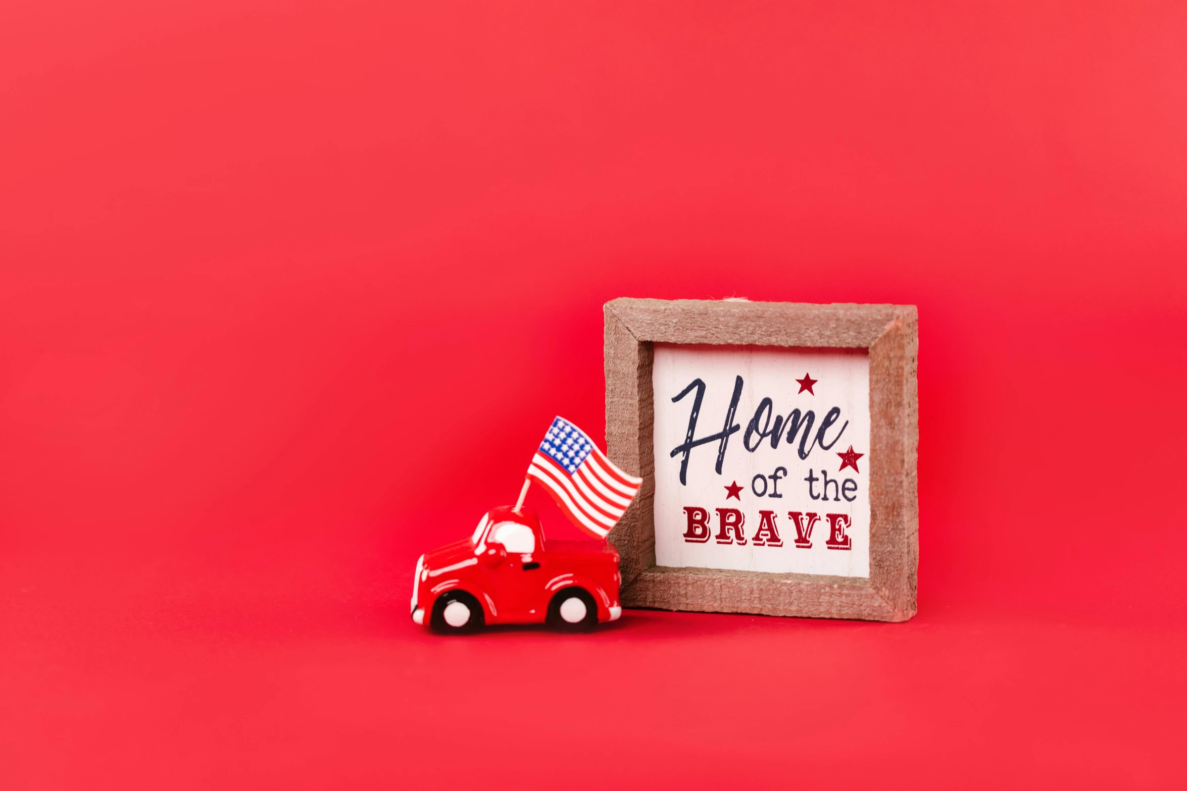 a toy car next to a sign that says home of the brave, pexels, folk art, background image, red white background, picture frames, wearing a red outfit