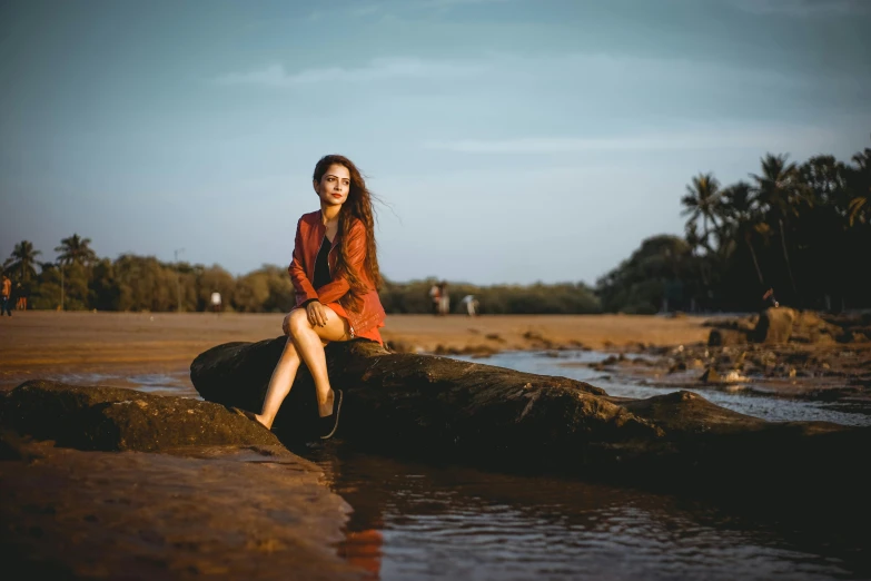 a woman sitting on a rock near a body of water, a portrait, by Max Dauthendey, pexels contest winner, indian girl with brown skin, red sand, [ cinematic, casually dressed