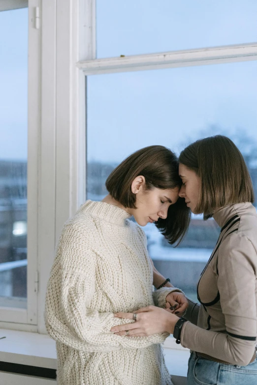 two women standing next to each other in front of a window, trending on pexels, romanticism, wearing turtleneck, comforting, lesbian, ( ( theatrical ) )