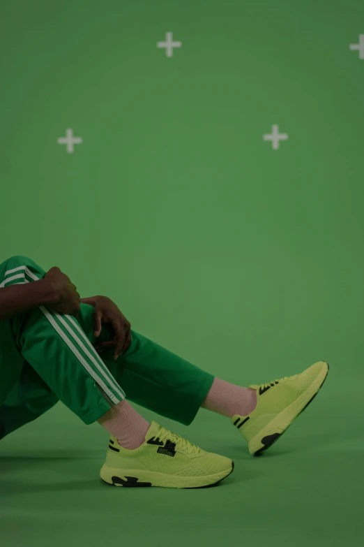 a man sitting on the ground in front of a green screen, by Attila Meszlenyi, adidas, adut akech, animation key shot, painted pale yellow and green