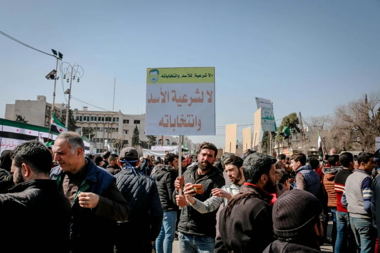 a group of people that are standing in the street, pexels, hurufiyya, subject action : holding sign, damascus, square, february)