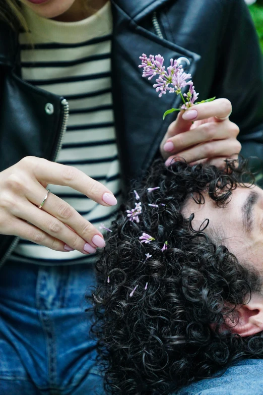 a woman sitting next to a man with a flower in his hair, trending on pexels, curls on top of his head, lilacs, transplanted hand to head, organic detail