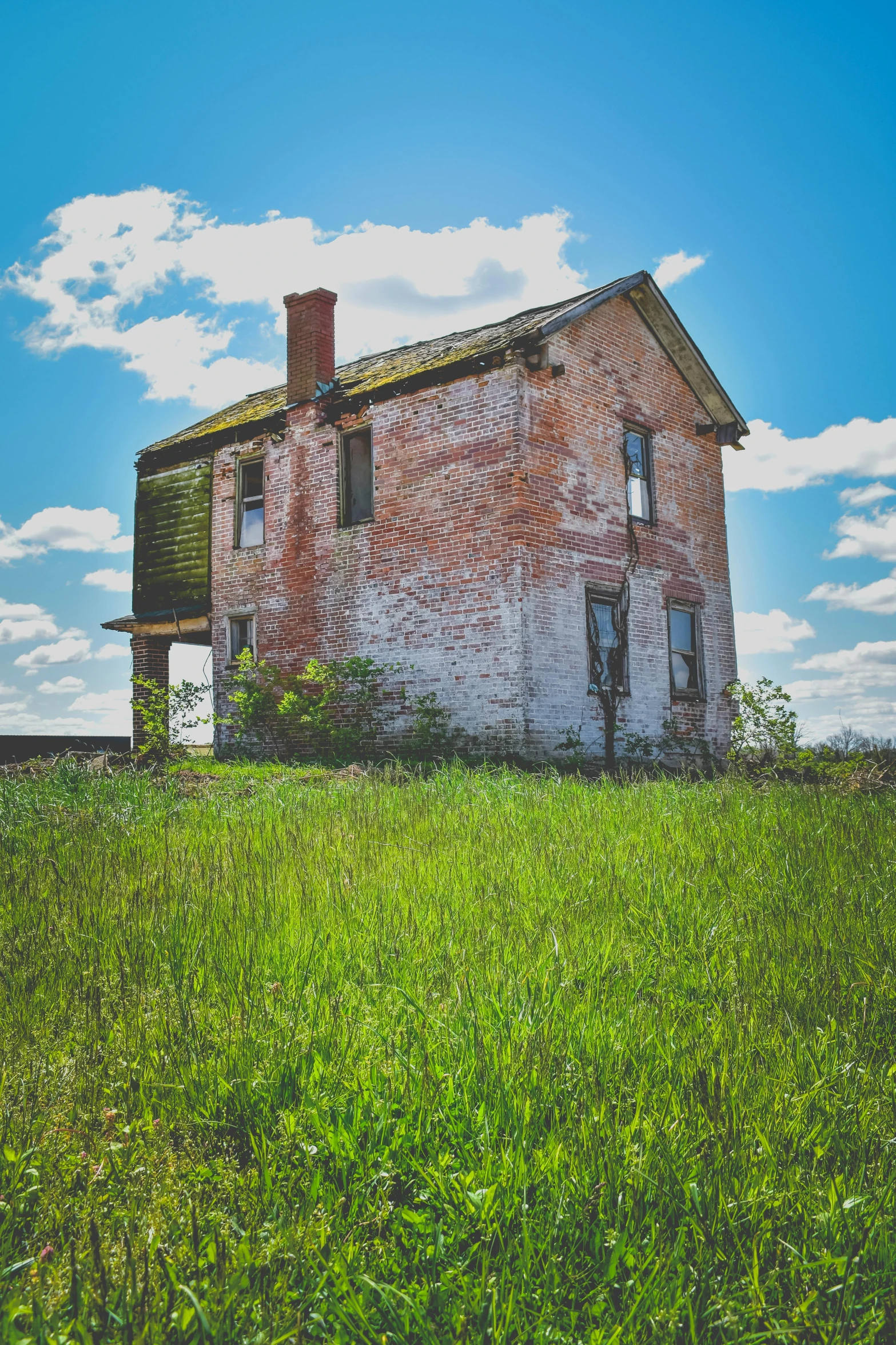 a red brick house sitting on top of a lush green field, a colorized photo, pexels contest winner, rotting, big sky, head shot, on a desolate plain