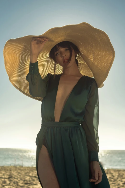 a woman standing on top of a sandy beach, an album cover, unsplash, renaissance, green hat, haute couture fashion shoot, evening sun, tan complexion