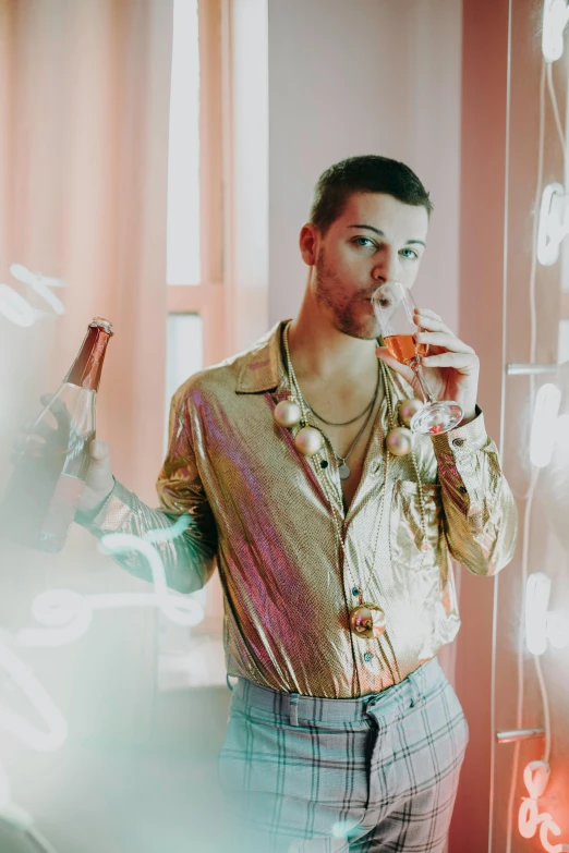 a man standing in front of a mirror holding a drink, an album cover, inspired by Elsa Bleda, trending on pexels, gold shirt, non binary model, bubbles, attractive man