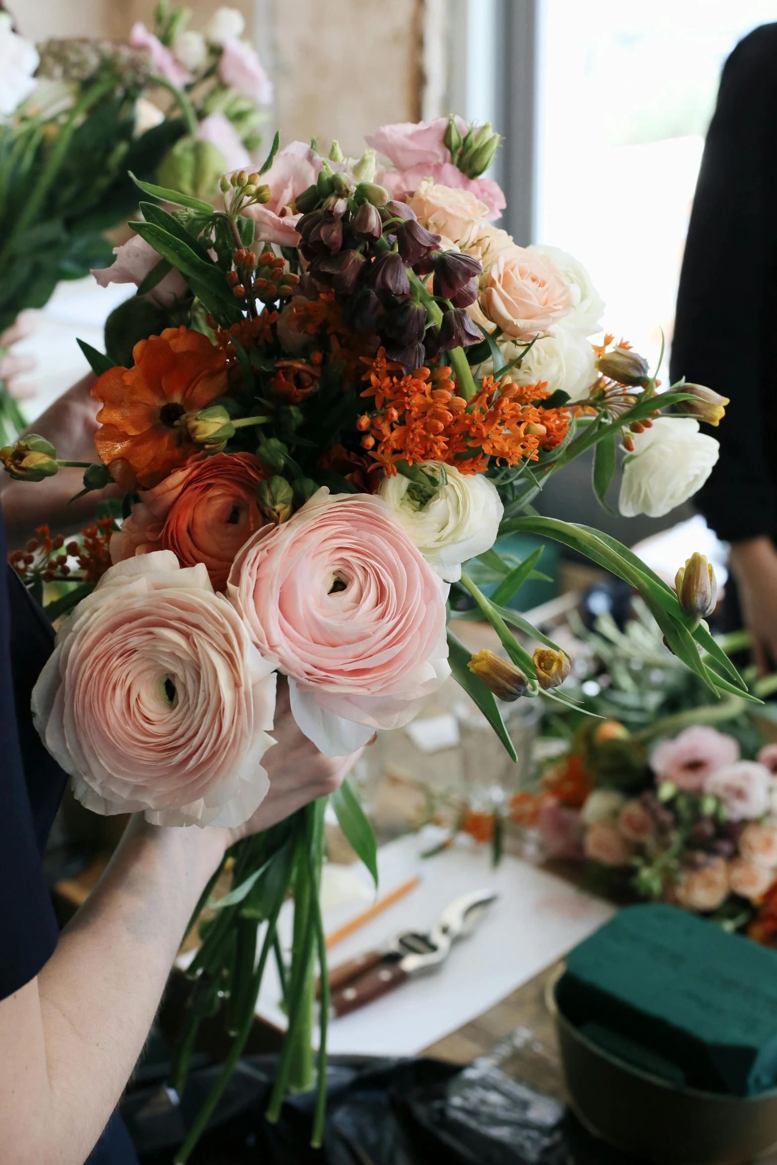 a woman holding a bunch of flowers in her hands, a still life, featured on instagram, pink orange flowers, carefully crafted, hands on counter, swirling around