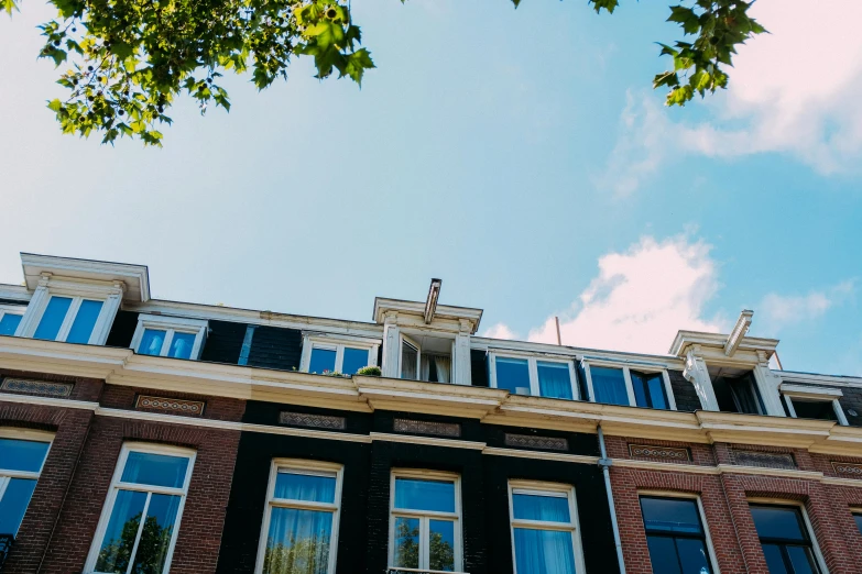 a tall brick building with lots of windows, by Jacob Toorenvliet, unsplash, neoclassicism, light blue sky, white houses, background image, dutch camera view