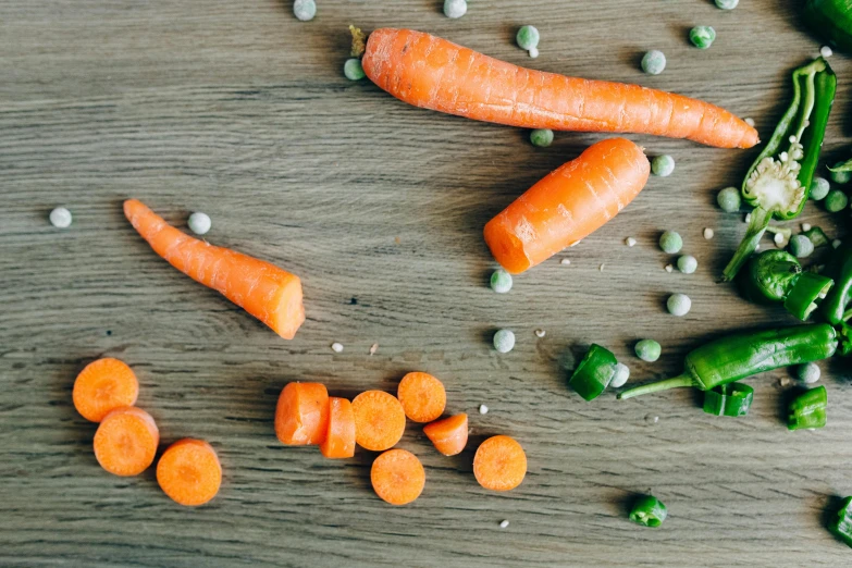 a wooden table topped with carrots and peas, by Julia Pishtar, unsplash, food particles, 1970s photo, background image