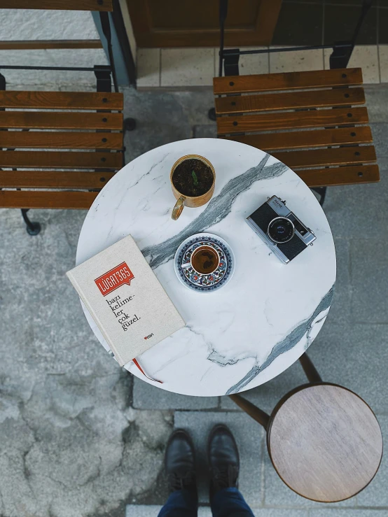 a person sitting at a table with a book and a cup of coffee, inspired by Louis Stettner, unsplash contest winner, hyperrealism, on a large marble wall, cafe racer, [ overhead view of a table ]!!, round format