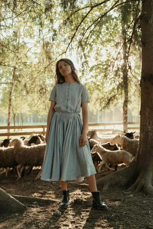 a woman standing in front of a herd of sheep, unsplash, renaissance, light blue dress portrait, with a tree in the background, wearing farm clothes, midi skirt