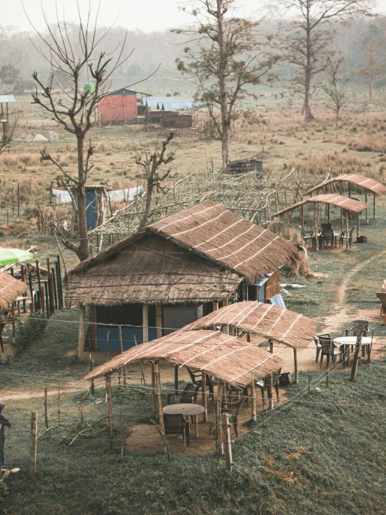 a group of huts sitting on top of a lush green field, trending on unsplash, bengal school of art, people sitting at tables, muddy village square, background image, temporary emergency shelter