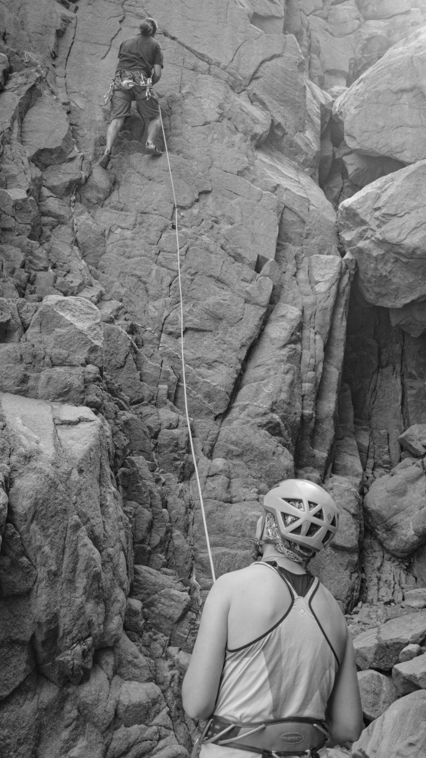 a black and white photo of a man on a rock climbing, hanging rope, helmet view, clyde aspevig, panoramic shot