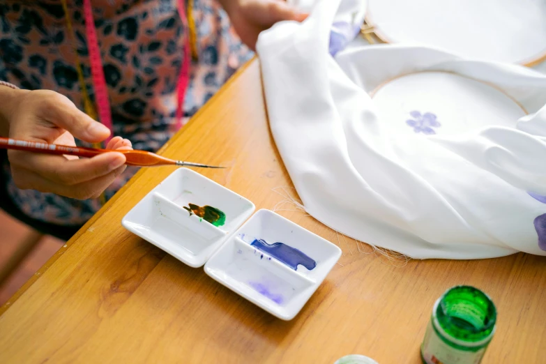 a close up of a person painting on a wooden table, an airbrush painting, inspired by Qi Baishi, trending on pexels, fabric embroidery, a purple fish, white, cloth accessories