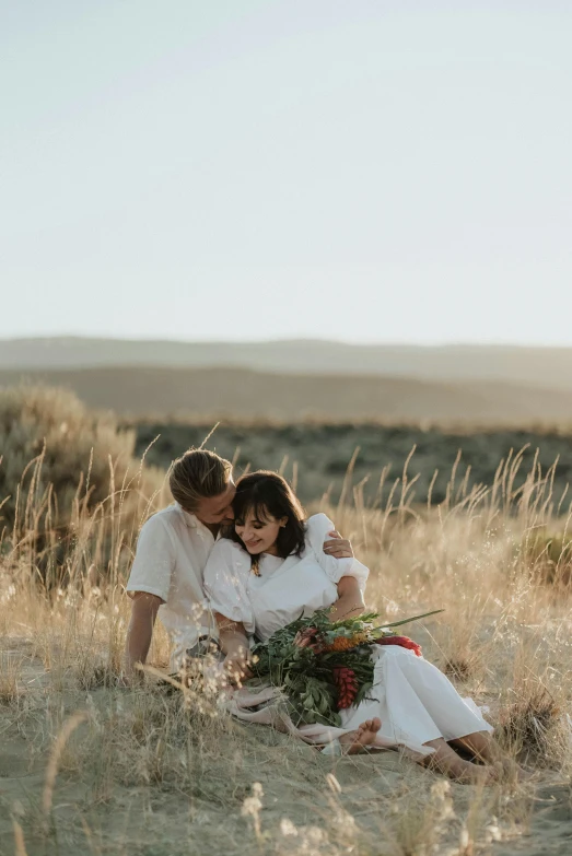 a man and woman sitting next to each other in a field, a picture, by Jessie Algie, trending on unsplash, romanticism, desert setting, bouquet, white, tender