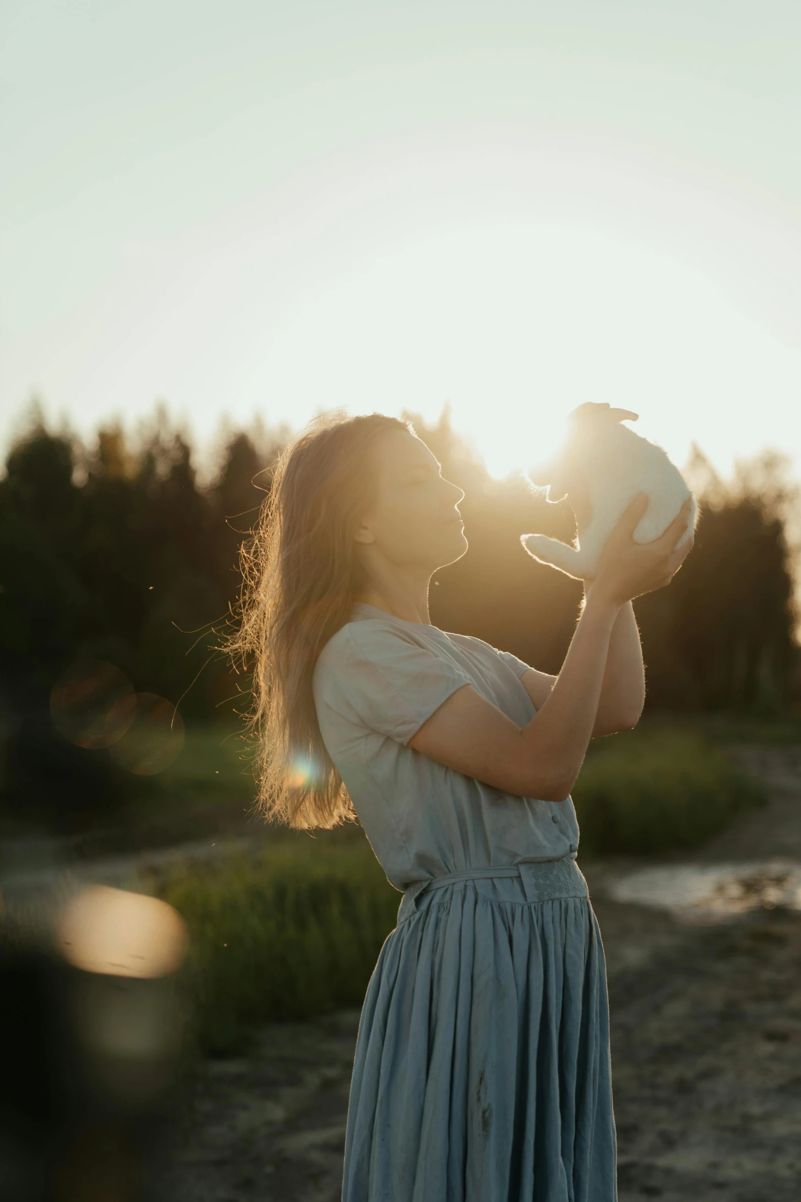 a woman in a blue dress drinking out of a cup, pexels contest winner, romanticism, sunset halo behind her head, holding a rabbit, play of light, maternal