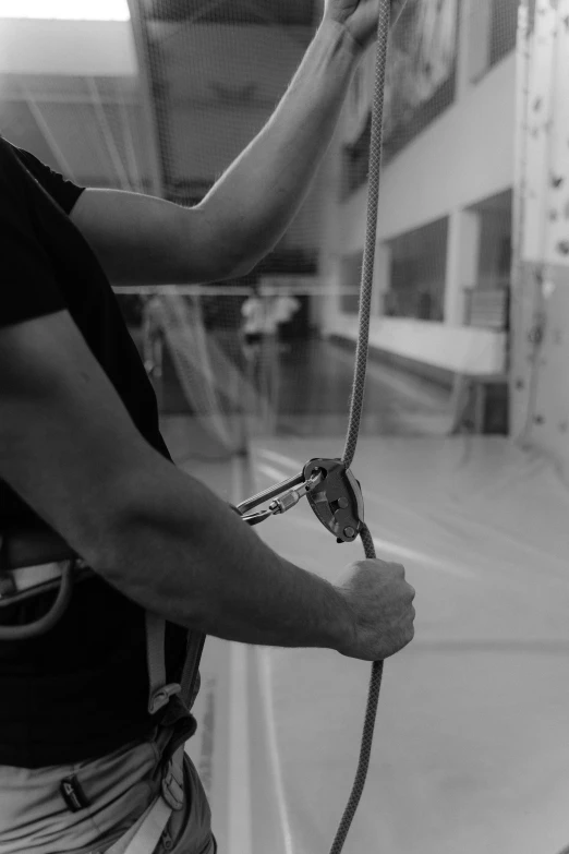 a black and white photo of a man holding a rope, in a gym, climber, smooth contours, webbing