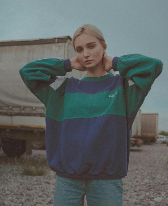 a woman standing in front of a truck, an album cover, inspired by Elsa Bleda, unsplash, realism, wearing a green sweater, green and blue colors, she is wearing streetwear, warm tri - color