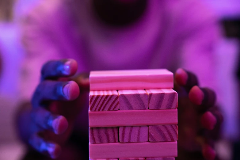 a close up of a person holding a stack of wooden blocks, by Lee Loughridge, unsplash, process art, bright pink purple lights, pink skin, ( ( dark skin ) ), performance