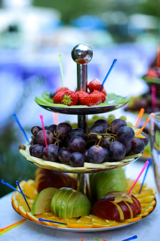 a table topped with three tiered trays filled with fruit, up close, grape, stems, fruit celebrity