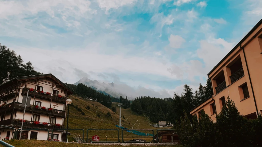 a tall building sitting on top of a lush green hillside, by Sebastian Spreng, pexels contest winner, : psychedelic ski resort, view from the street, panorama view of the sky, vintage vibe