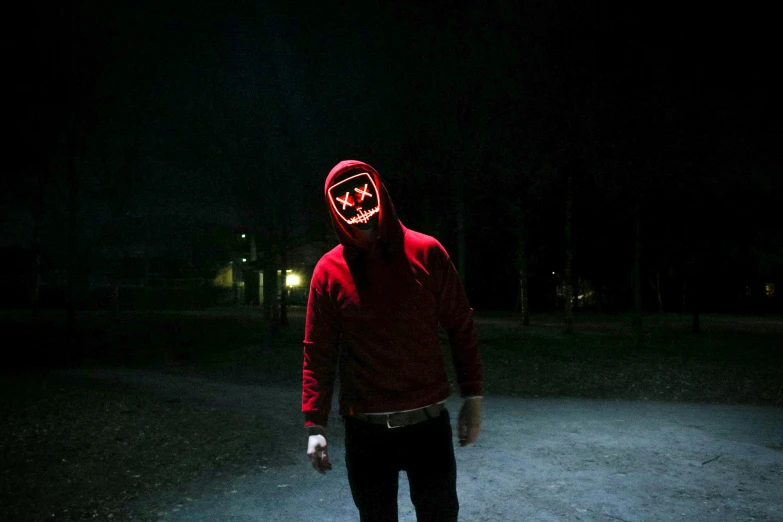 a man in a red hoodie standing in the dark, an album cover, pexels, robot ghost mask, outdoors at night, led, leds