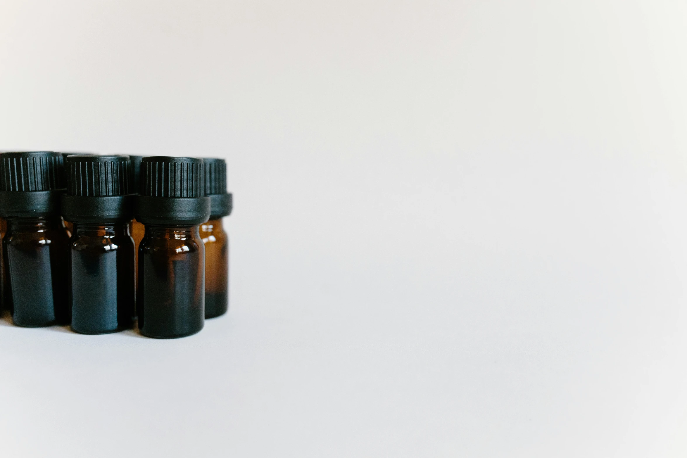 a group of bottles of essential oils on a white surface, by Emma Andijewska, unsplash, visual art, minimalist photorealist, brown, low quality footage, shot on sony a 7