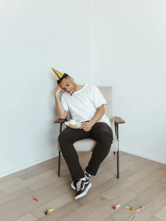 a man sitting in a chair with a party hat on, postminimalism, happily tired, gold shirt, 2019 trending photo, wearing pants