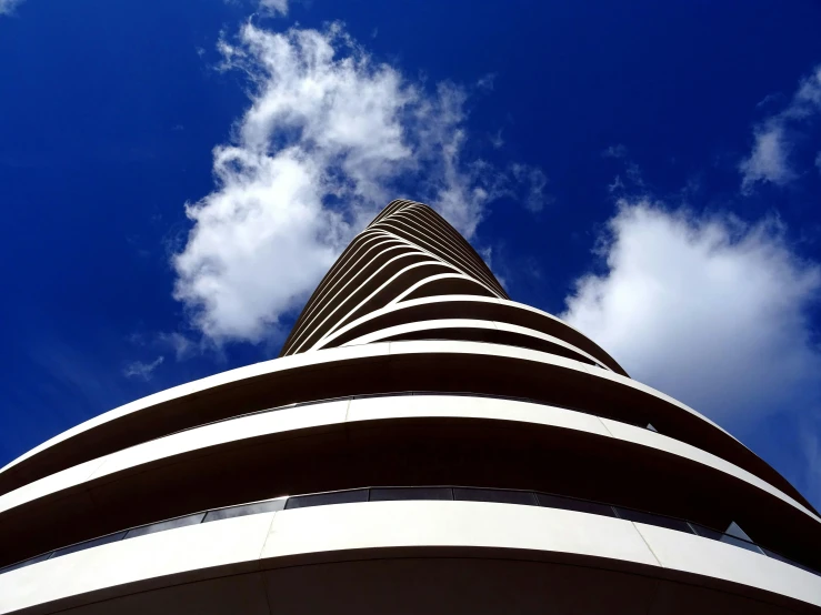 a tall building with a blue sky in the background, inspired by Zha Shibiao, unsplash contest winner, brutalism, spiral clouds, costa blanca, taken in the mid 2000s, 8k resolution”