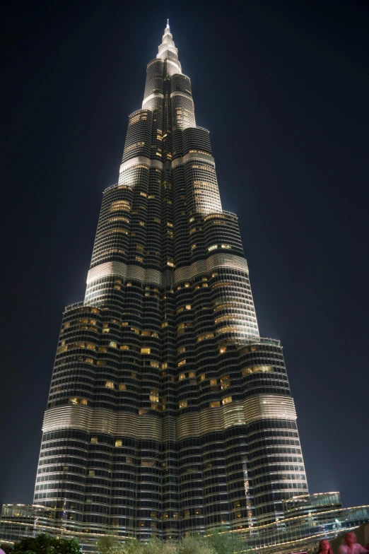 a very tall building lit up at night, dubai, towering high up over your view, seen from outside