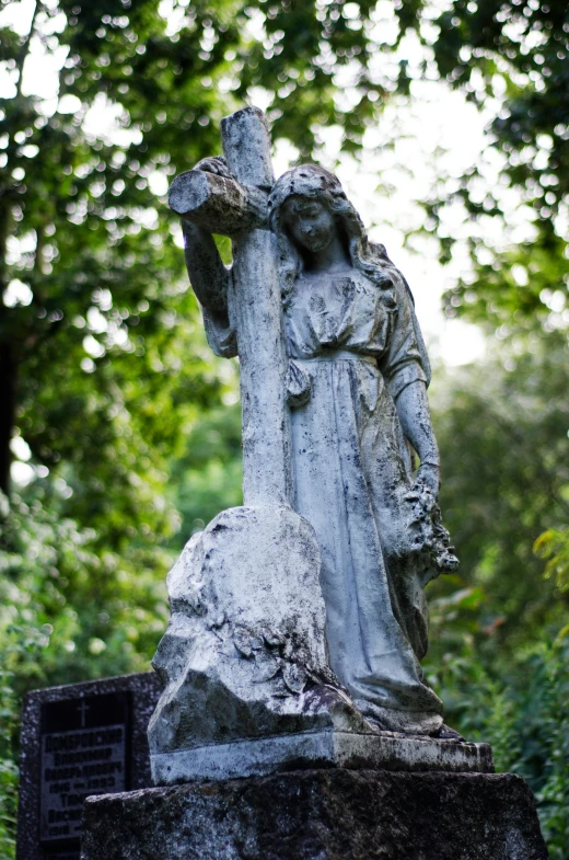 a statue of a woman holding a cross in a cemetery, inspired by Eleanor Fortescue-Brickdale, romanticism, july 2 0 1 1, grey, cross