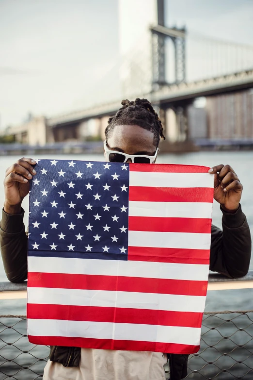 a woman holding an american flag in front of a bridge, a picture, by Samuel Washington Weis, trending on unsplash, black man, playboi carti portrait, covered in, 🚿🗝📝