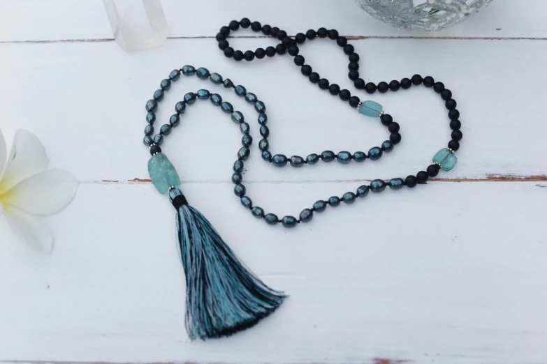 a close up of a beaded necklace with a tassel, by Rachel Reckitt, unsplash, black and teal paper, padmasana, morning mist, black pearls