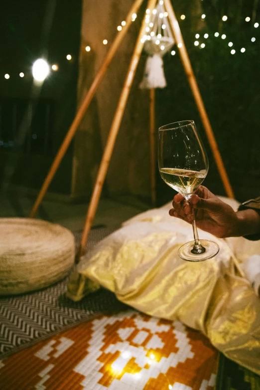 a woman sitting on the ground holding a glass of wine, inspired by Elsa Bleda, trending on unsplash, renaissance, teepee, gold linens, moroccan, medium shot taken from behind